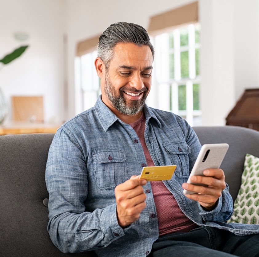 Dark haired man on sofa with phone and credit card online banking