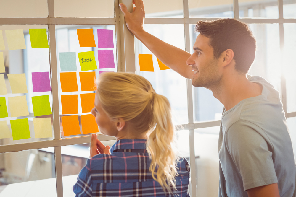 Man and woman smiling and looking at wall of coloured post it notes